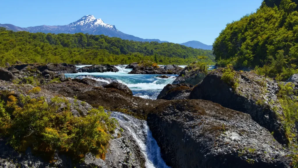 Petrohué River waterfalls among volcanic rocks with a snow-capped volcano in the background, Los Lagos Region, Chile