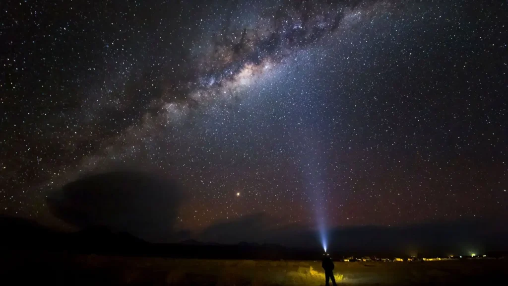 The Milky Way over the Atacama Desert at night, with a person lighting up the starry sky with a flashlight