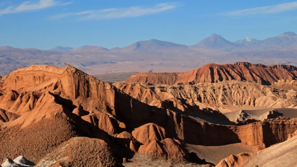Brown rocky formations of the Valley of the Moon with volcanoes in the background, in San Pedro de Atacama, Chile